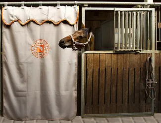 Beige Childéric stable curtain with logo in front of a stall