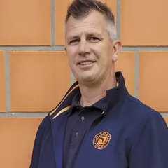 Tibor Balogh in dunkelblauer Childéric Jacke vor einer Ziegelwand
