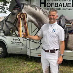Bernd Hofbauer mit Schimmel und Siegerschleife vor seinem Pferdetransporter